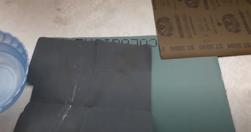 Расположите наждачную бумагу на стекле